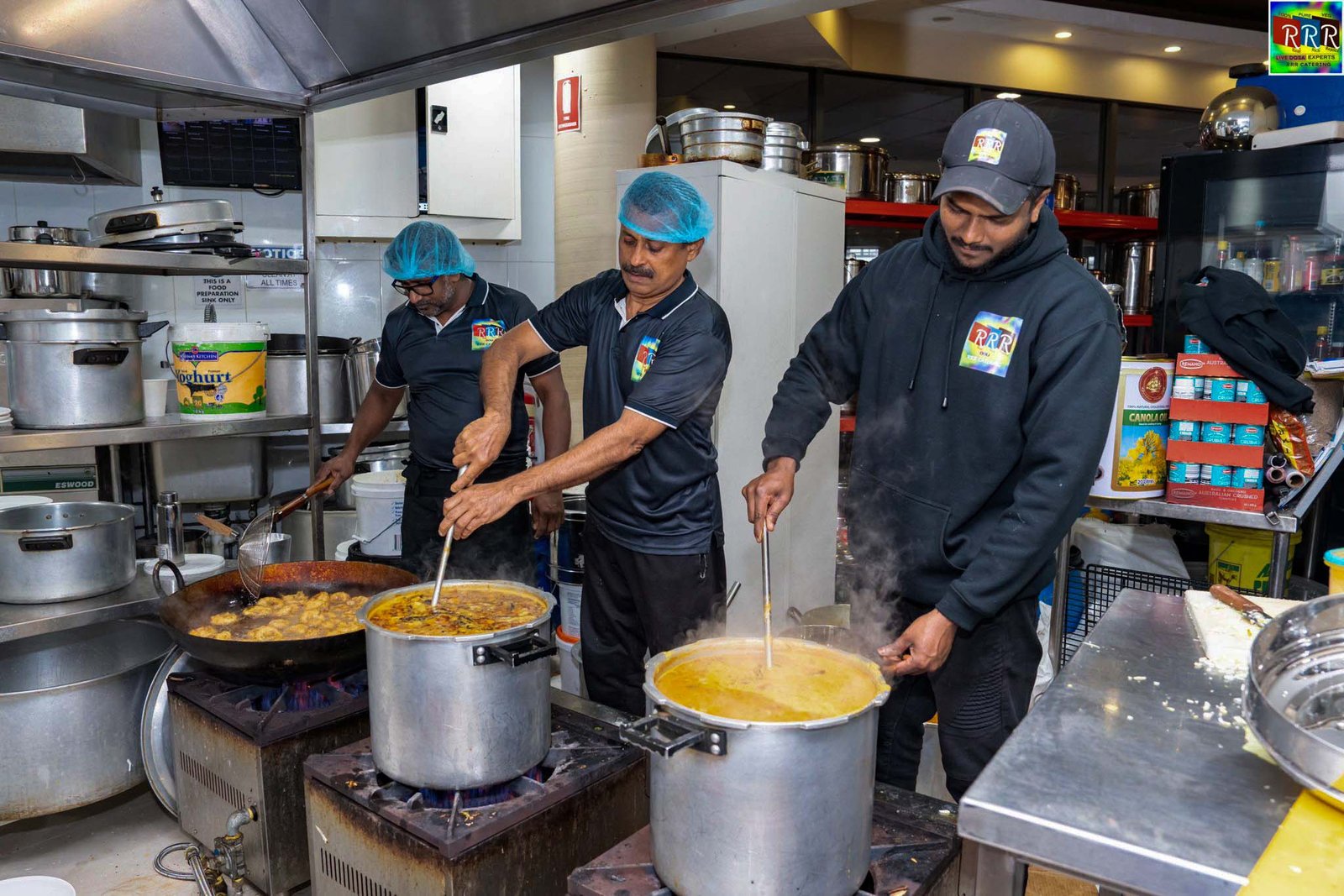 RRR Live Catering Service staff in branded uniforms cooking in a commercial kitchen for an event