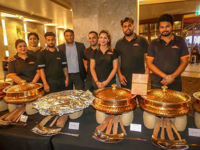 Taj Indian Restaurant catering team in branded uniforms with copper serving dishes at a Sydney event